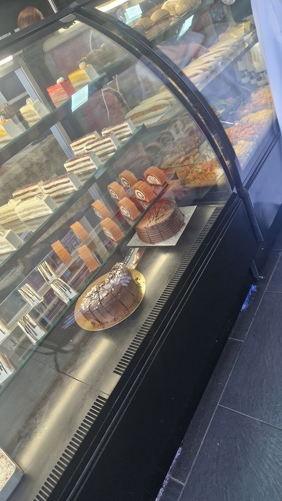The glass cake cabinet from an angle, rows of individual cakes with the shop floor behind.