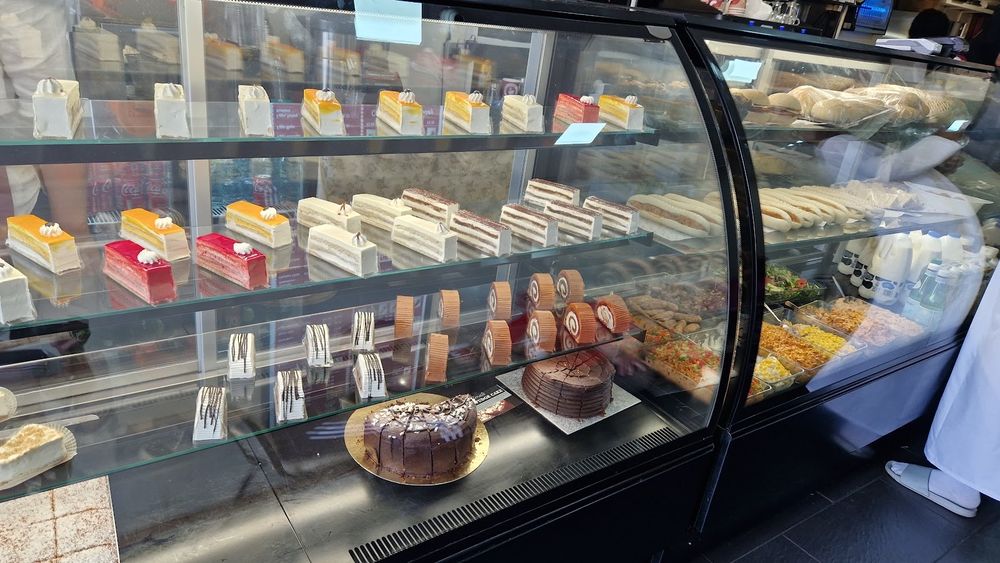 The curved glass patisserie counter filled with rows of cakes and slices.