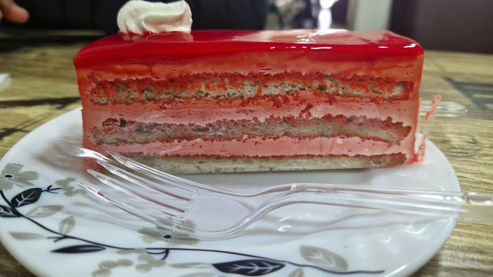 A slice of strawberry gateau on a patterned plate on a wooden table.